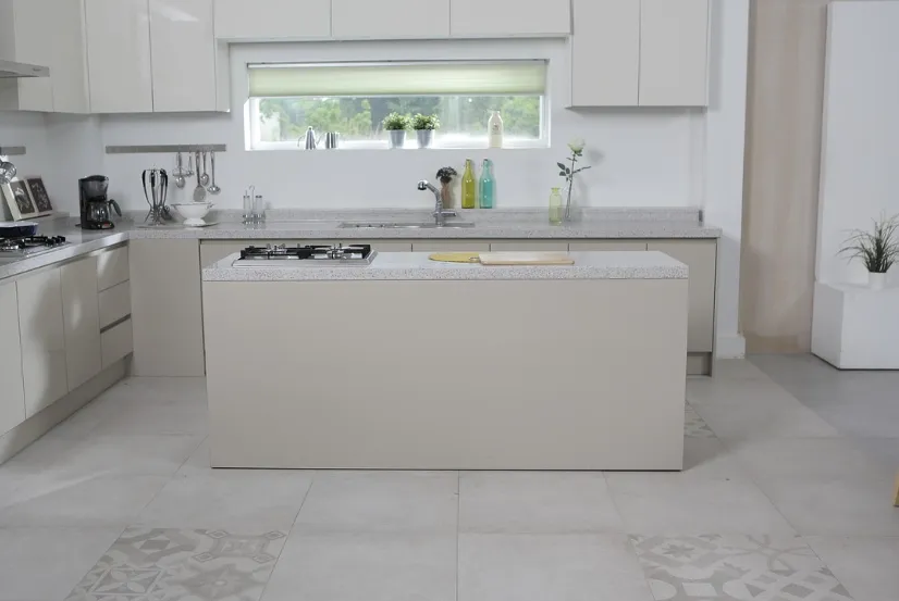 Modern white kitchen with a central island, built-in stove, countertop appliances, and large window with green plants on the sill.