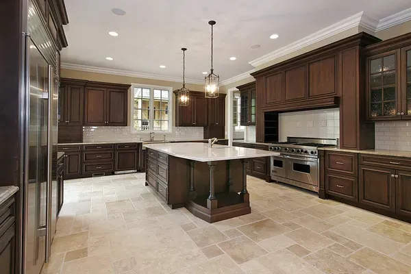 Spacious kitchen with dark wood cabinets, tile floor, large central island, stainless steel appliances, pendant lights, and beige subway tile backsplash.