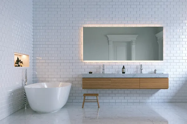 Modern bathroom with white subway tile walls, a freestanding bathtub, a floating double sink vanity with a marble top, a backlit mirror, and a small wooden stool.