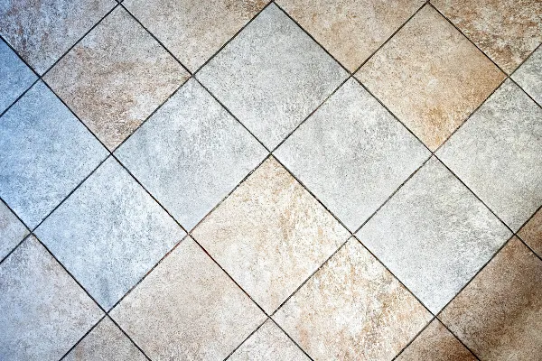 Square ceramic floor tiles arranged in a diagonal pattern, displaying a mix of beige, light brown, and light gray colors.