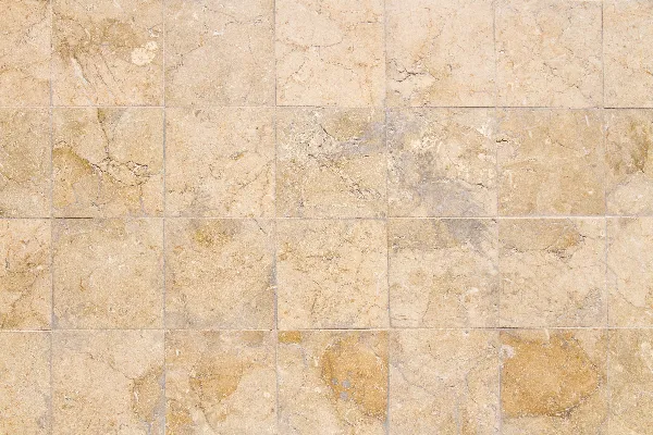A close-up view of a beige stone tile wall with a grid pattern, showing natural textures and subtle color variations.