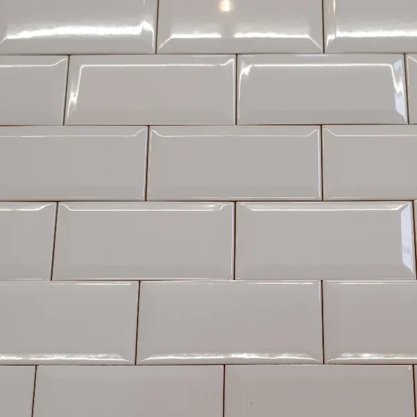Close-up of a wall with white rectangular subway tiles arranged in a staggered brick pattern with visible grout lines.